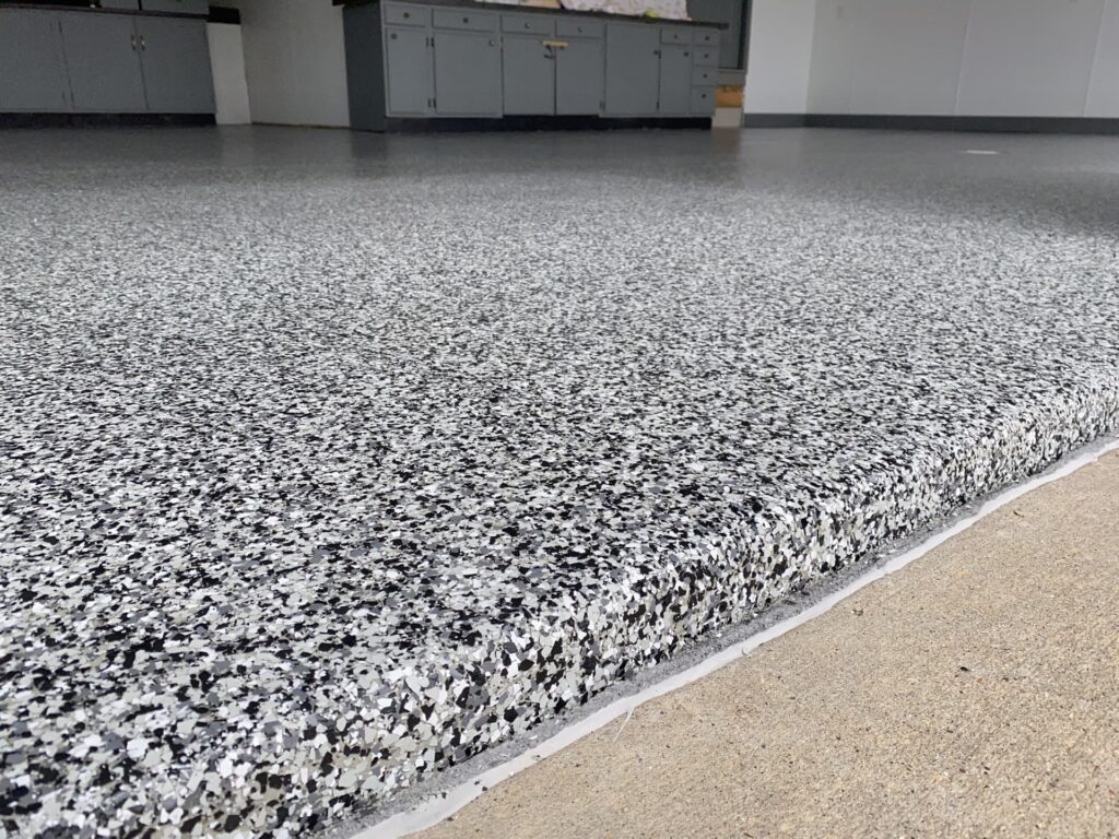 Close-up of a speckled, newly-installed epoxy floor in a room with cabinets. The image primarily focuses on the textured flooring.