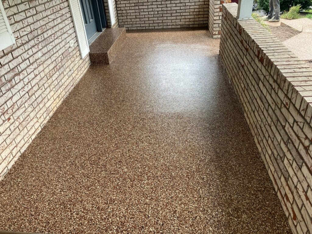 A front porch with speckled flooring and brick walls; a person stands in the background near a garden path.