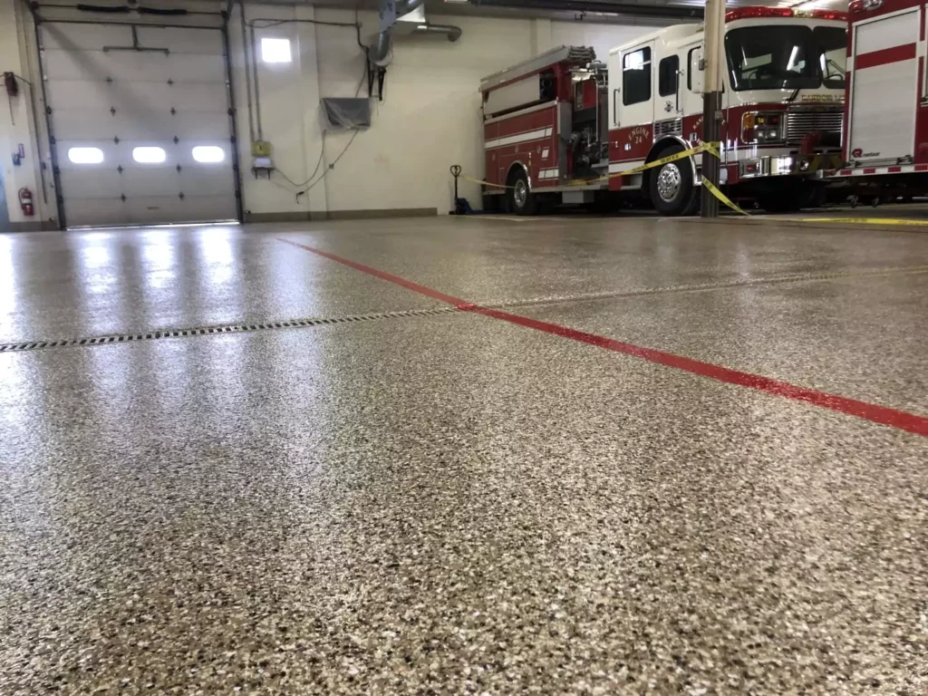 A fire truck is parked inside a clean, well-lit garage with polished floors, red lines, and an overhead door.